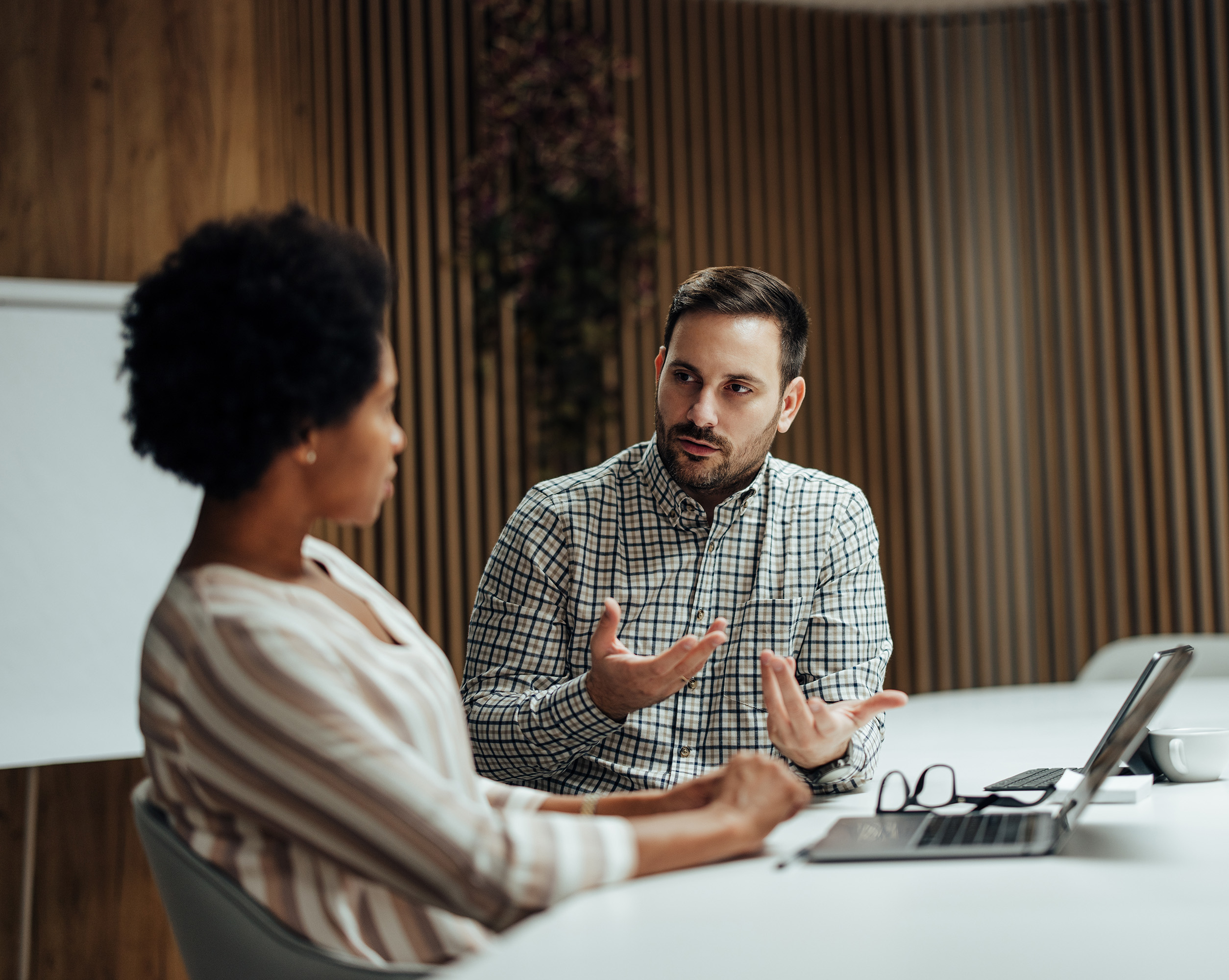 A man is hosting a meeting with a female client talking about an employee benefits package and why it's time to go back to basics.