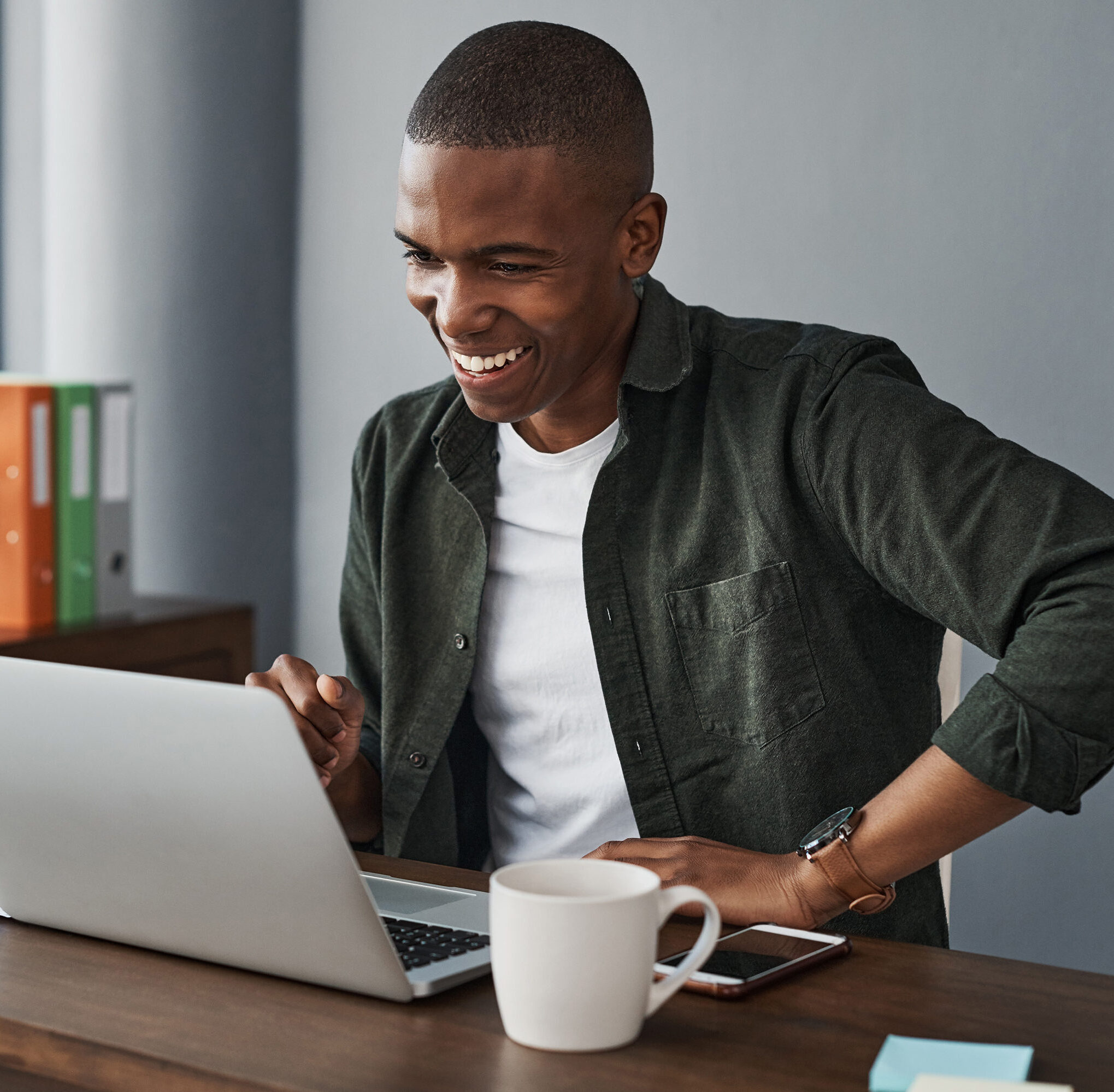 This image is based on our Software & Technology services, with an employee on a call on his laptop. The employee is working from a home office, he's wearing a white t-shirt, green shirt over the top and a smile on his face.